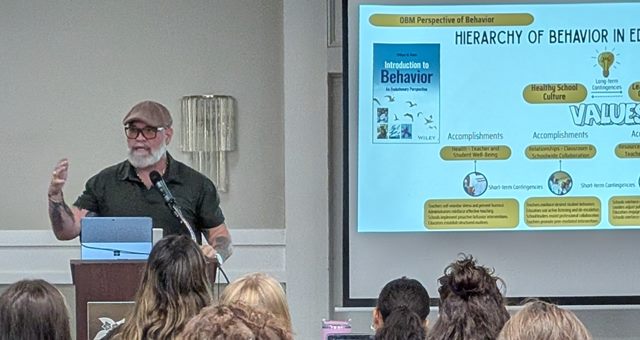 Dr. Gavoni presenting a slide on the hierarchy of behavior in education to a seated audience